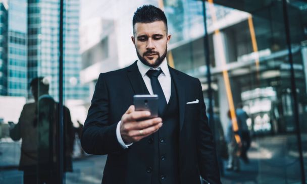Serious executive manager 30 years old looking news on smartphone reading email about business using mobile phone with 4G internet near building in financial district, concept of online business - Photo, Image