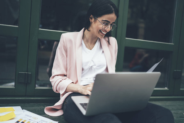 Happy young emotional entrepreneur feeling excited and happy of working process making job great outdoors, successful smiling hipster girl in spectacles e learning with modern netbook and papers - 写真・画像