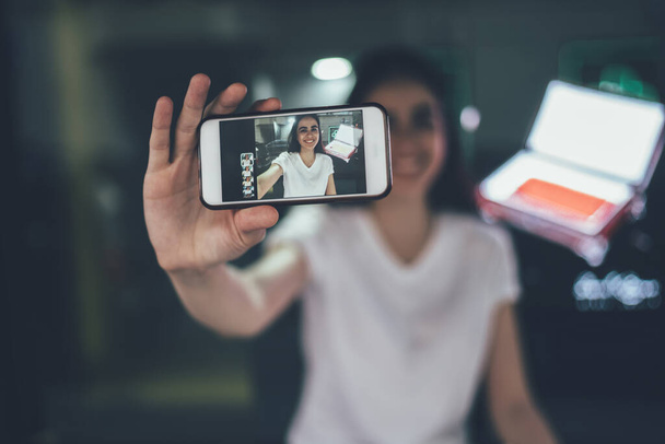 Selective focus on modern cellphone gadget holding positive millennial hipster girl, woman using main camera on smartphone device for photographing herself and attracting followers with publication - Foto, Bild