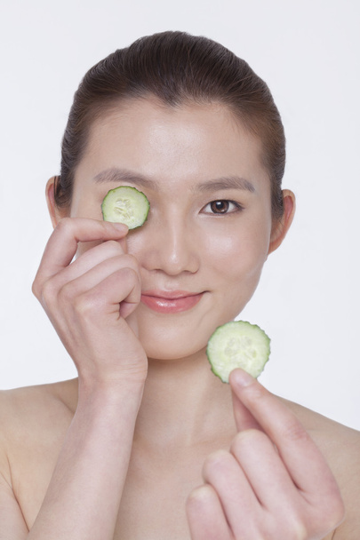 Woman holding up cucumber slices to put over her eyes - Photo, Image
