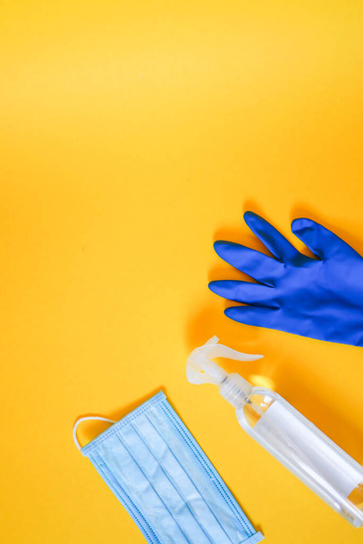 Handschuhmaske und Desinfektionsmittel in der Ecke des gelben Hintergrunds - Foto, Bild