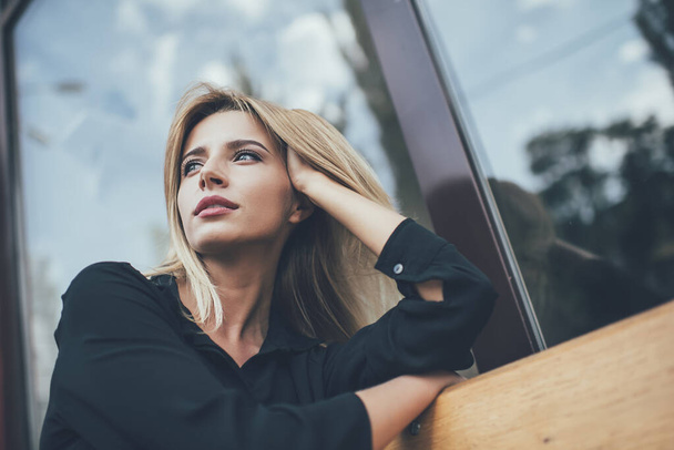 Below view of pondering woman dressed in stylish black shirt thougthful looking away and thinking on ideas, attractive hipster girl in casual clothing lost in thoughts during rest time on city bench - Foto, imagen