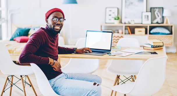 Portrait of african american hipster guy enjoy new software for netbook with mock up screen working on freelance at home, cheerful man looking at camera satisfied with earning money on laptop at fla - 写真・画像
