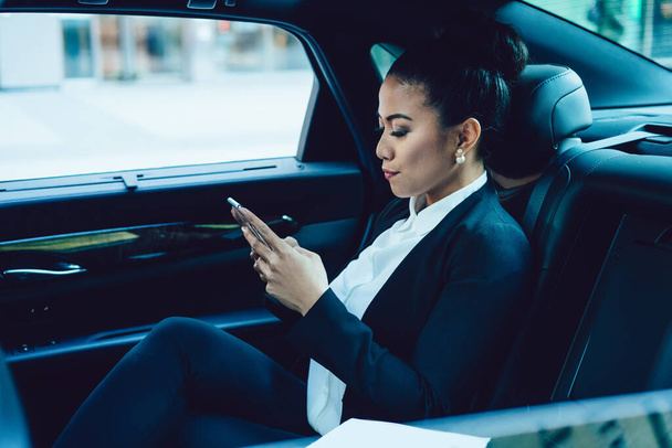 Side view of serious woman checking information on financial website interested on company statistics connected to 4g internet in car, attractive female employer using smartphone for online work - Foto, Bild