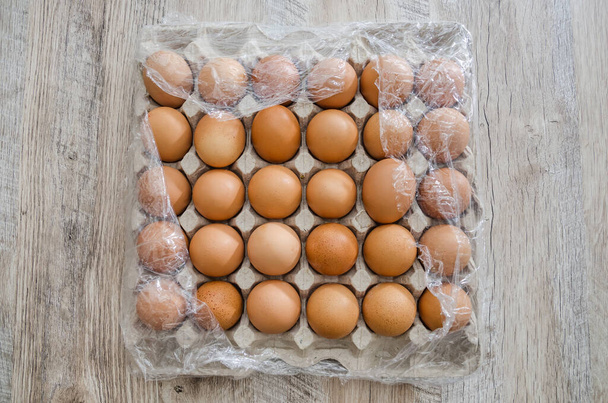 Csirketojás kartondobozban, műanyag fóliába csomagolva egy fa asztalon. - Fotó, kép