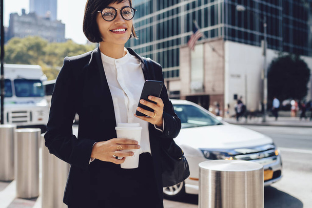 Half length portrait of cheerful female proud ceo in optical spectacles looking at camera during coffee break on urban setting in New York city, happy woman trader in elegant suit enjoying time - Фото, зображення