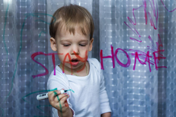 Adorable toddler girl attaching rainbow drawing to window glass as sign of hope. Creative games for kids staying at home during lockdown. Self isolation and coronavirus quarantine concept - Photo, Image
