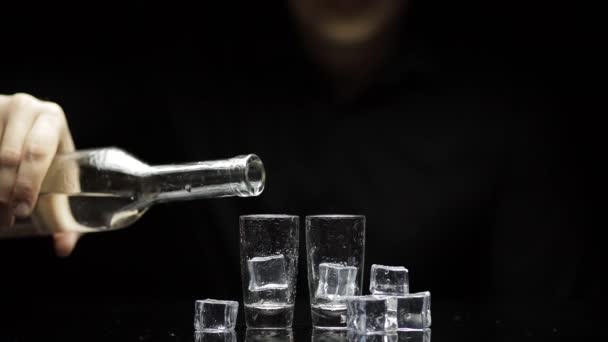 Barman vierta el vodka congelado de la botella en dos vasos con hielo. Fondo negro
 - Metraje, vídeo