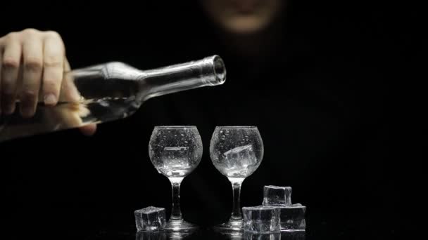 Barmann gießt gefrorenen Wodka aus der Flasche in zwei Gläser mit Eis. Schwarzer Hintergrund - Filmmaterial, Video