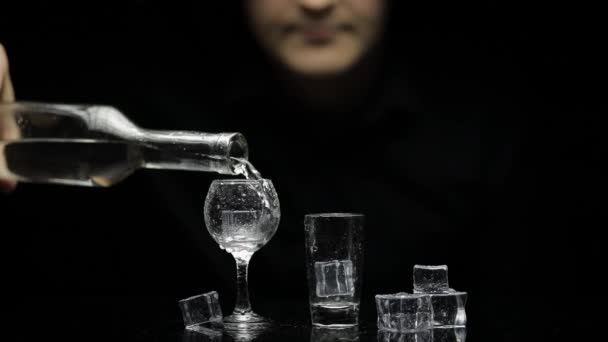Barman giet bevroren wodka uit de fles in twee glazen met ijs. Zwarte achtergrond - Video