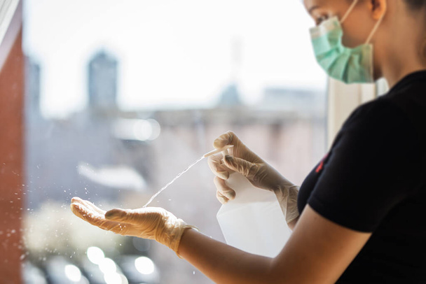 Meisje met beschermende handschoenen en suikermasker sprays vloeibare antibacteriële hand ontsmettingsmiddel om zichzelf te beschermen tegen coronavirus pandemie - Foto, afbeelding
