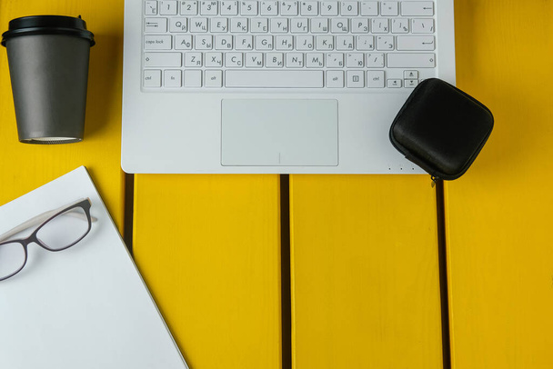 Composición plana con vasos, café, bloc de notas y portátil sobre un fondo de madera amarilla. Concepto de tarea
. - Foto, imagen