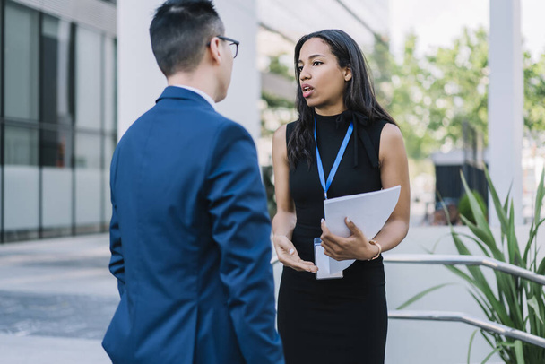 Elegant African American woman with id badge holding papers and talking to man while organizing meeting on business conference standing on street  - Fotó, kép