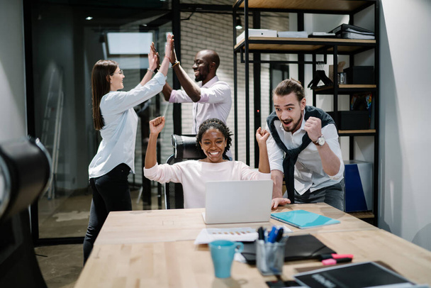 Happy successful business team looking at laptop screen reading received email with information about winning grand for startup project, multicultural colleagues feeling overjoyed at workplace - Foto, Imagen