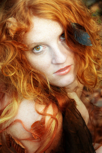 Portré egy aranyos, fiatal vörös hajú lányról, piros és narancssárga őszi levelekkel. Gyönyörű arc egy fiatal szexi nő között piros arany lombozat. - Fotó, kép