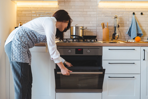 young pretty woman open oven to cook. domestic kitchen concept. copy space - Fotó, kép