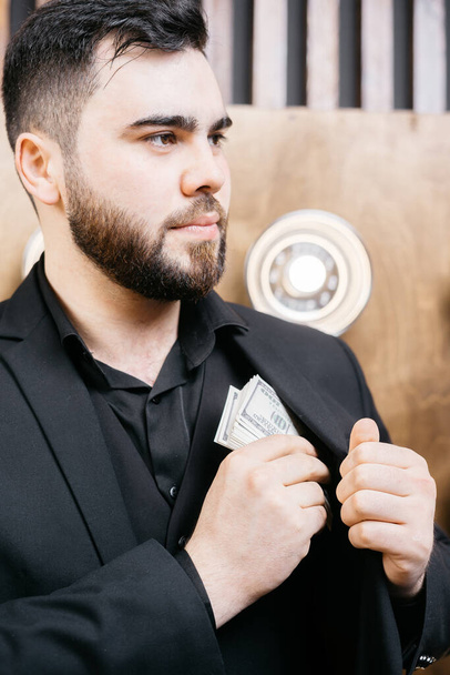 Egy szakállas fiatalember pénzt tesz a zsebébe. - Fotó, kép