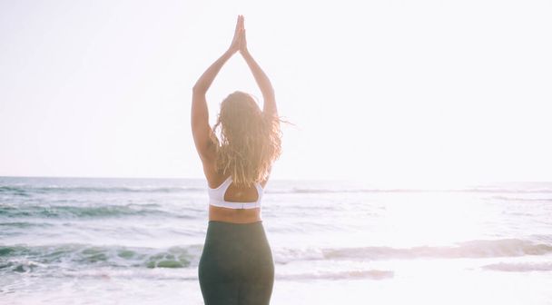 Young calm woman with hands up doing mountain pose for relieves chronic stress patterns enjoying morning training time on sea beach, concept of spirituality and recreation for minds and soul - Foto, afbeelding