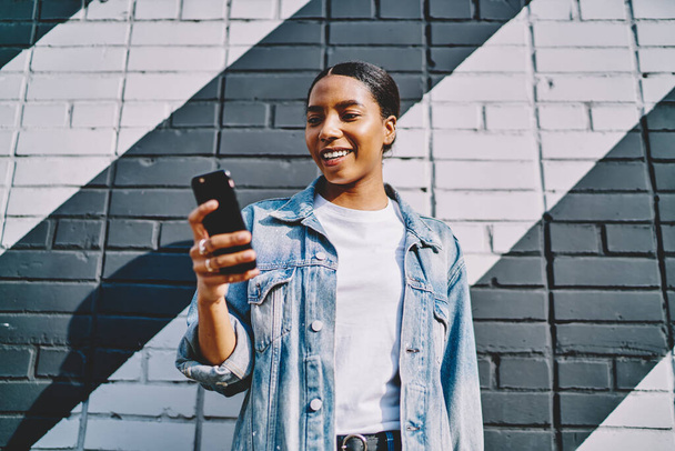 Below view of cheerful african american young woman happy with received notification from internet shop with big sales on smartphone device.Positive dark skinned chatting in social network on cellular - Foto, Imagen