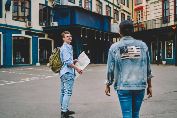 Back view of african american young woman in denim wear travel together with caucasian boyfriend in new city.Couple in love walking in urban setting of cozy town during weekend's trip - Φωτογραφία, εικόνα