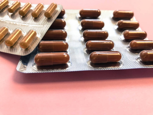 Medyczne farmaceutyczne brązowe leki do leczenia chorób i zabijania drobnoustrojów i wirusów tabletki i witaminy blistry z koronawirusem covid-19 na różowym tle - Zdjęcie, obraz