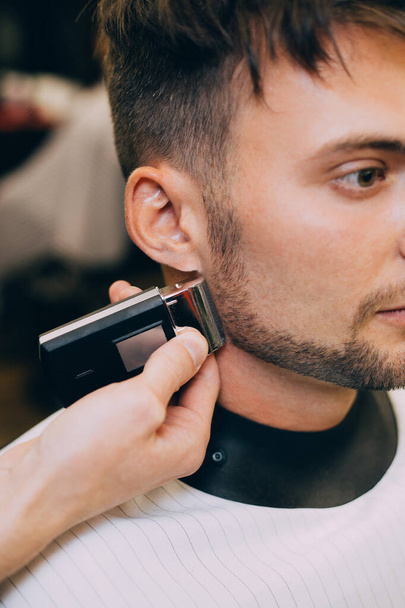 Portrait  man being trimmed with professional electric clipper machine in barbershop.Male beauty treatment concept. guy getting new haircut in barber salon. - Photo, image