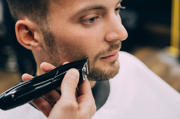 Portrait  man being trimmed with professional electric clipper machine in barbershop.Male beauty treatment concept. guy getting new haircut in barber salon. - Φωτογραφία, εικόνα
