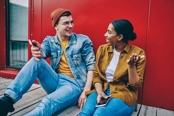 Cheerful multiracial male and female hipster guys in casual trendy wear discussing funny information from netbook resting on weekends, happy couple in love laughing at jokes sitting togethe - Foto, Bild