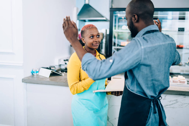 African American man gesturing with hands and telling interesting story to female colleague while standing near cafe counter during break together - Foto, Imagem