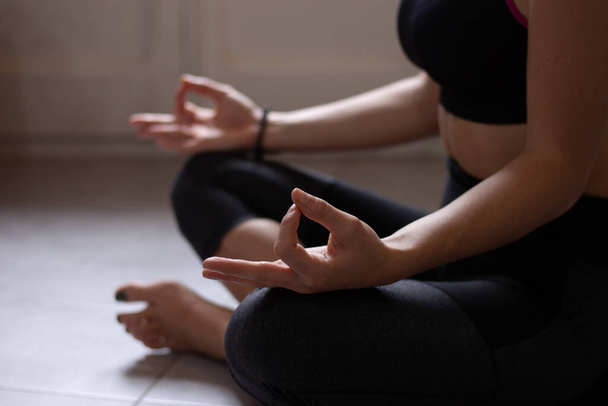 Vista de cerca de una joven anónima haciendo yoga matutino después de despertarse en casa. Modelo femenino sentado con las piernas cruzadas en pose Easy, postura Sukhasana y meditando
. - Foto, Imagen