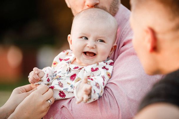 dad is holding little cute smiling daughter in arms. Family spending summer time together, outside, on vacation, outdoors on sunset. The concept of family holiday - Photo, Image