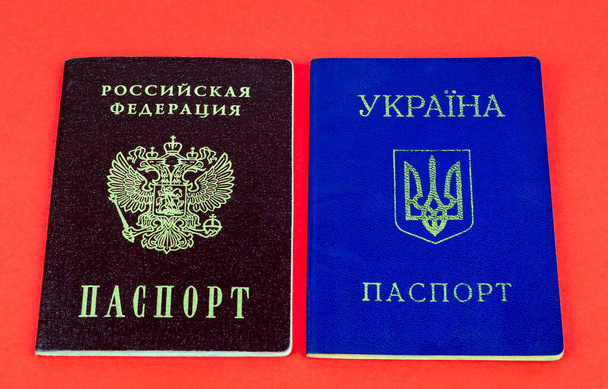 Twee nationale binnenlandse paspoorten, rood Russisch paspoort en blauw Oekraïens paspoort op rode achtergrond - Foto, afbeelding