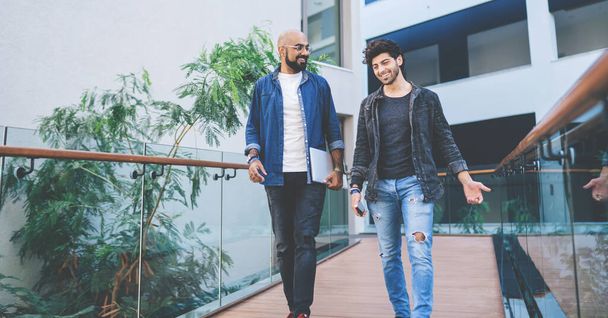 Contemporary modern ethnic men in casual clothing walking together on building pathway and talking friendly while having meeting about new startup - Фото, зображення