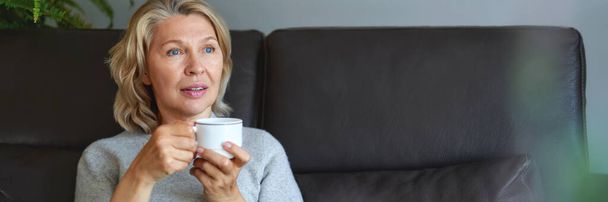 femme âgée assise sur le canapé dans son salon et tenant une tasse de café
. - Photo, image