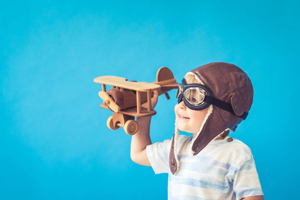 Boldog gyermek játszik vintage fa repülőgép. A srác jól szórakozik a kék háttér ellenére. Képzelet és szabadság fogalma - Fotó, kép