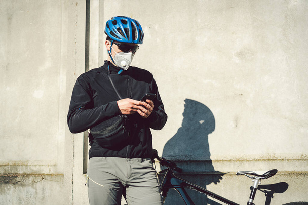 A biciklis futár megállt, és nézte a telefonos alkalmazást. Küldemény a karanténban. Egy férfi a lélegeztetőgépben mobilt használ. Kerékpárfutár munkák. - Fotó, kép
