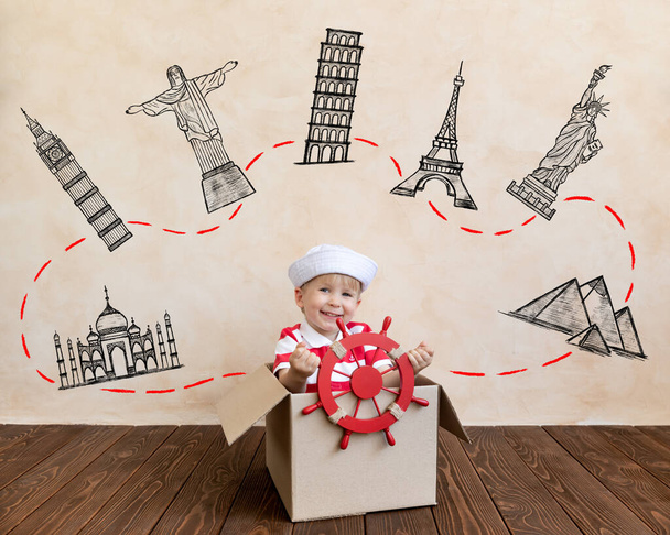 Happy child dreams of becoming a captain. Kid having fun at home. Boy wearing striped shirt playing in cardboard box. Summer vacation and travel concept. Seven wonders of the world - Photo, Image