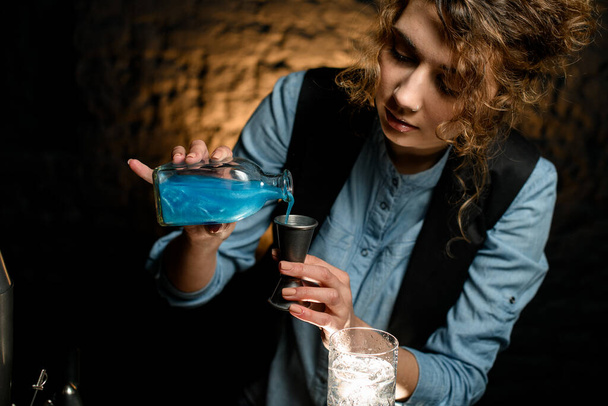 female bartender pours bright blue liquor into metal jigger. - Foto, immagini