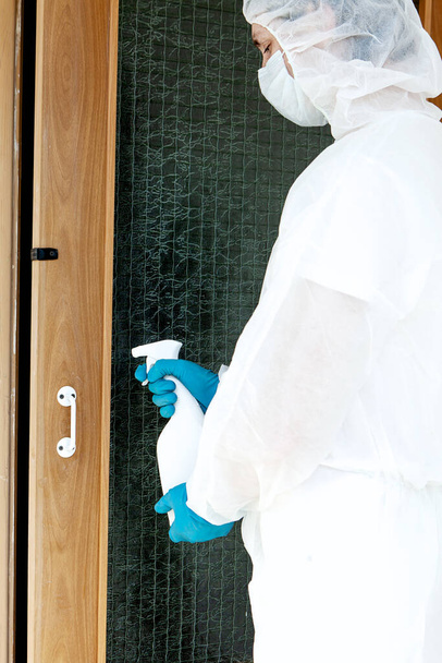 A man in a protective suit gloves and face mask holding a spray. Concept of antibacterial treatment in a public place - Photo, Image