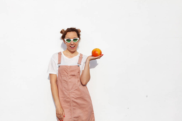 Студийный портрет счастливой девушки, весело улыбающейся, держа в руках спелый грейпфрут, стоящий изолированно на белом фоне. Вкусные тропические фрукты, здоровая пища, сырая пища - Фото, изображение