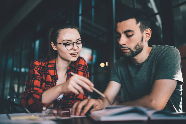 Contemporary casual woman in glasses and man sitting together at table and reading paper document while coworking on new idea - Фото, зображення