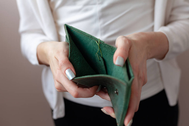 A girl in a protective mask holds a purse. Green purse in women's hands. The concept of poverty and bankruptcy - Photo, Image