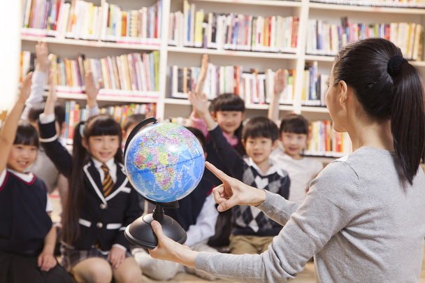 Teacher teaching geography to schoolchildren with a globe - Photo, Image