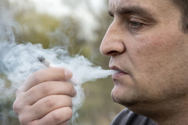 Portret uliczny człowieka, który pali jointa i wydycha papierosa.Koncepcja: rekreacja na świeżym powietrzu, relaks z pomocą konopi indyjskich, unikanie problemów, uspokajanie nerwów. - Zdjęcie, obraz