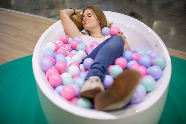 若い白人の女の子が多色のプラスチックボールでお風呂に横になって目を閉じて笑っています。密接なソフトフォーカス - 写真・画像