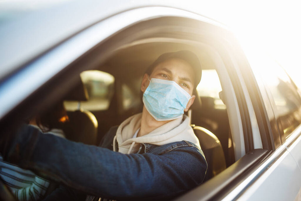 Man driving a car wearing sterile medical mask. Taxi driver with a passanger stuck in a traffic jam during coronavirus quarantine isolation in the city. Prevernt spread of covid-19 concept - Photo, Image