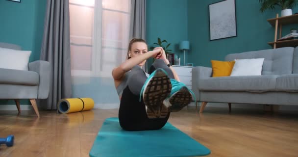 Female fitness trainer in athletic top doing abdominal exercises in modern apartment. Fit woman doing abs exercises flexing legs on floor at home. Fitness, home, exercising and diet concept. - Video, Çekim