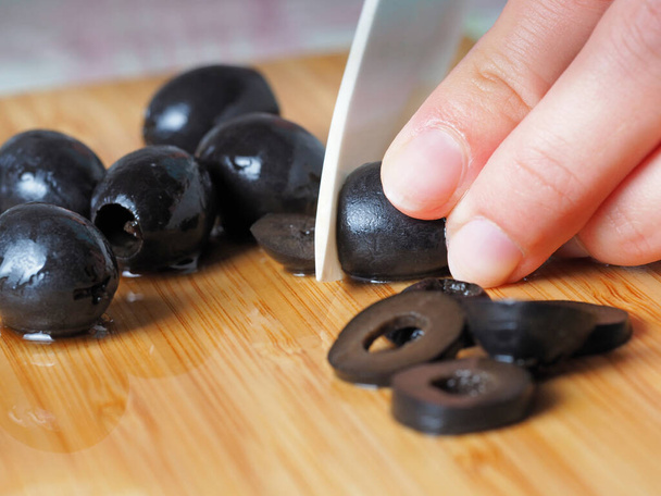 Les olives noires sont coupées en gros plan avec un couteau tranchant
. - Photo, image