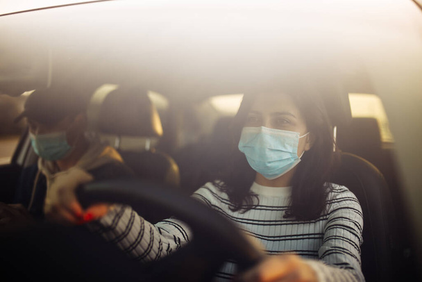 Boy and girl driving a car wearing sterile medical mask. Taxi driver with a passanger stuck in a traffic jam during coronavirus quarantine isolation in the city. Prevernt spread of covid-19 concept - Photo, Image