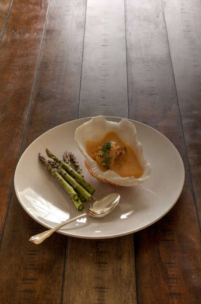 Harina de mariscos de sopa de bizcocho de langosta en un tazón de concha marina en un plato blanco con espárragos
. - Foto, Imagen